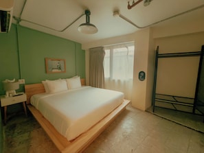 Una habitación de hotel con cama, mesita de noche, lámpara, ventana con cortinas y puerta.