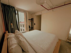 Un dormitorio con una cama grande, una ventana con cortinas, una lámpara colgante y vistas a un edificio exterior.
