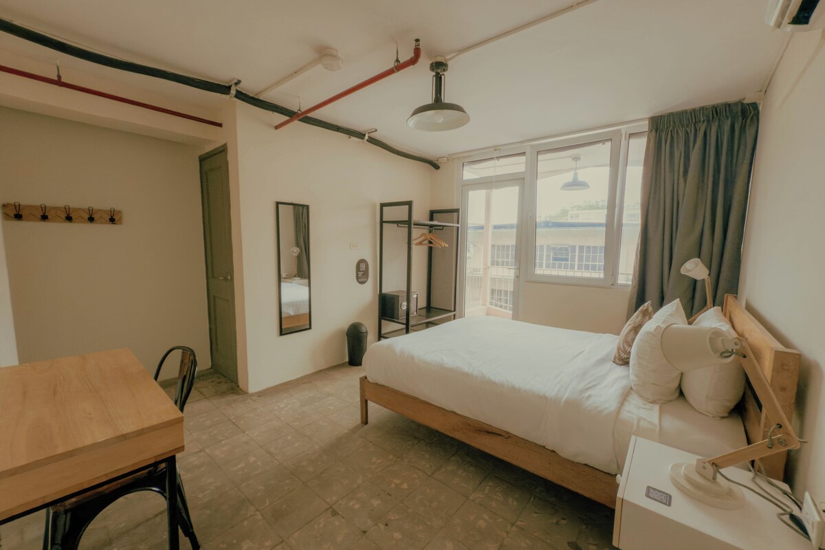 Un dormitorio con cama, mesita de noche, lámpara y ventana con cortinas.