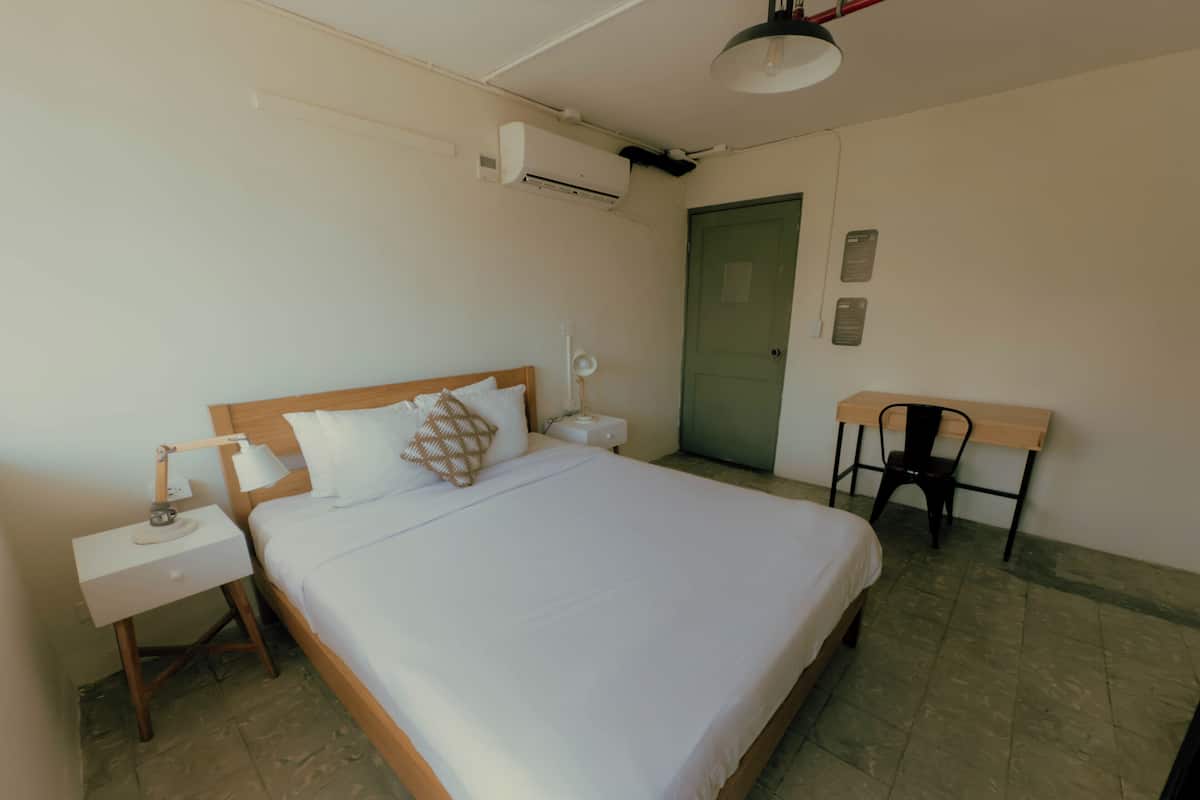 Een keurig opgeruimde hotelkamer met een bed, nachtkastje, lamp, stoel en een airconditioner.