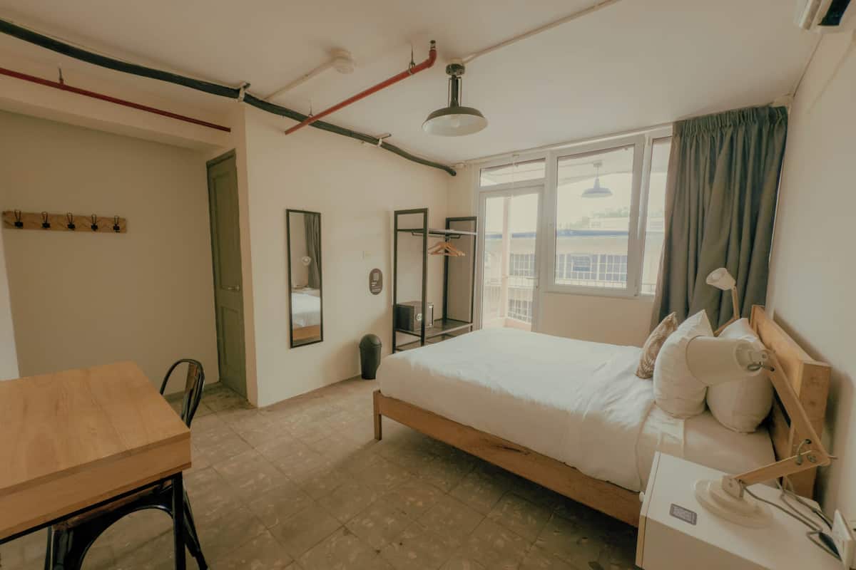 Een slaapkamer met een bed, nachtkastje, lamp en een raam met gordijnen.