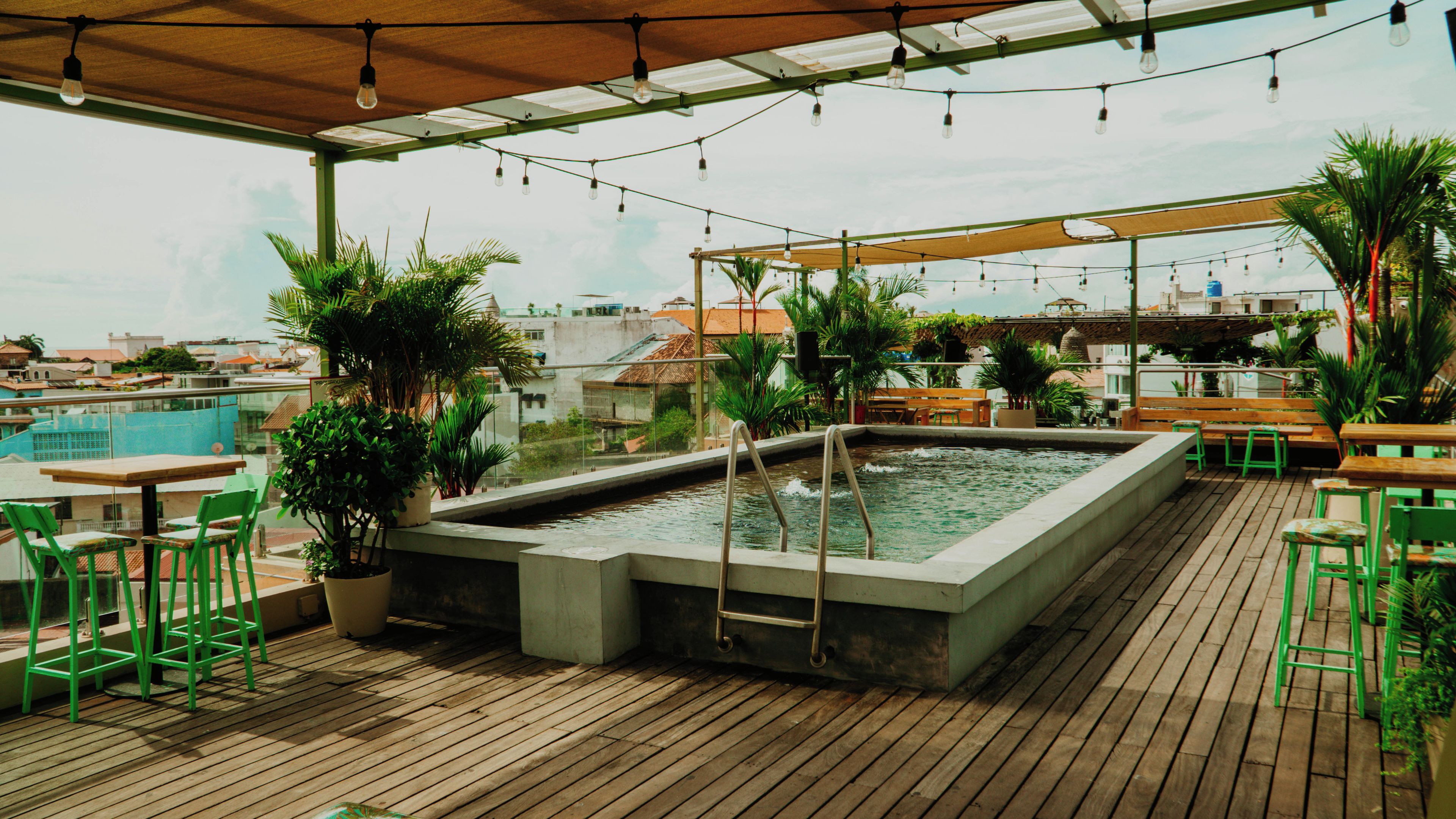 Un espace extérieur avec une piscine, une terrasse en bois, des chaises vertes et des plantes en pot.