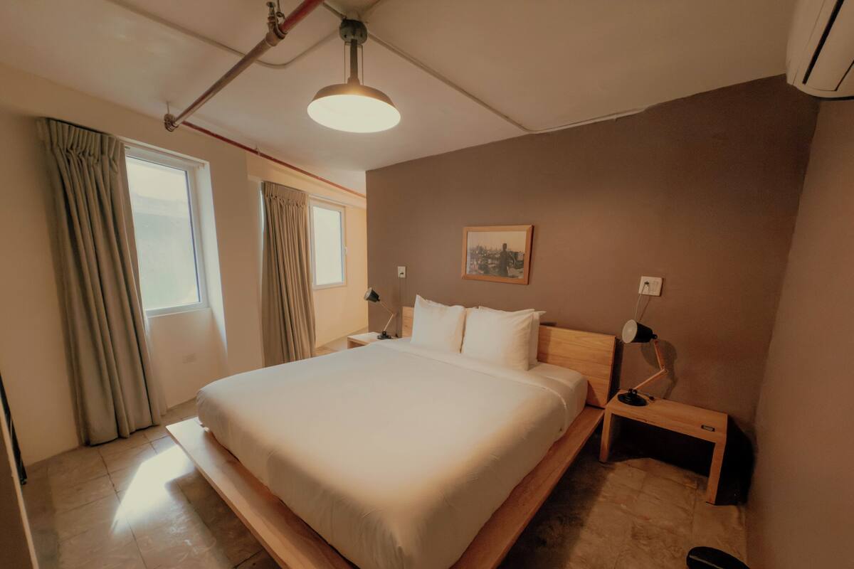 Een moderne hotelkamer met een groot bed, nachtkastjes, een plafondlamp en een raam met gordijnen.