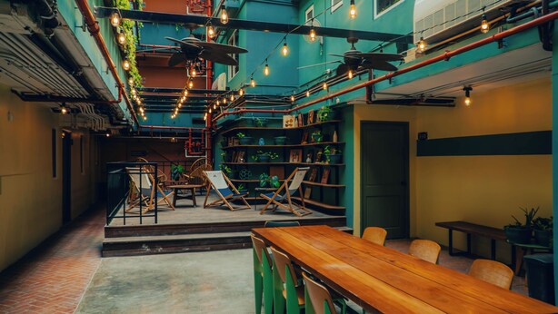 A cozy cafe with wooden tables and chairs, a brick floor, and a green wall with shelves of plants and books. - Viajero Panama (Panama City)