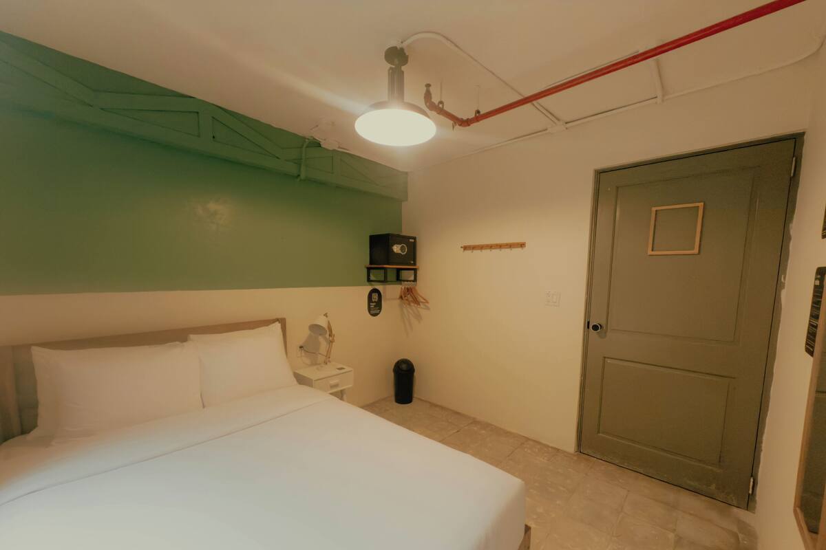 Slaapkamer met een bed, nachtkastje, wandplank, deur en een plafondlamp.