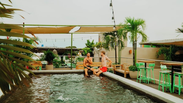 Dos hombres sentados junto a una piscina, rodeados de follaje y mobiliario exterior.