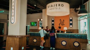 Una recepción en ViaJero Hostels con un diseño moderno, que incluye un cartel grande y una pantalla de televisión.