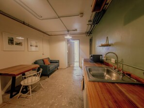 Cocina compacta con encimera de madera, un lavamanos y una zona de comedor con una silla y una mesa.