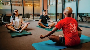 Three people sitting on yoga mats in a room with large windows and a view of the outside. - Viajero Panama (Panama City)