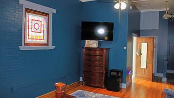A room with a blue wall, a wooden dresser, a television, and a ceiling fan.