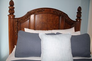A bed with a wooden headboard, multiple pillows, and a plain wall in the background. - Villagio Luxury Shops And Hotel (Pittsburgh)