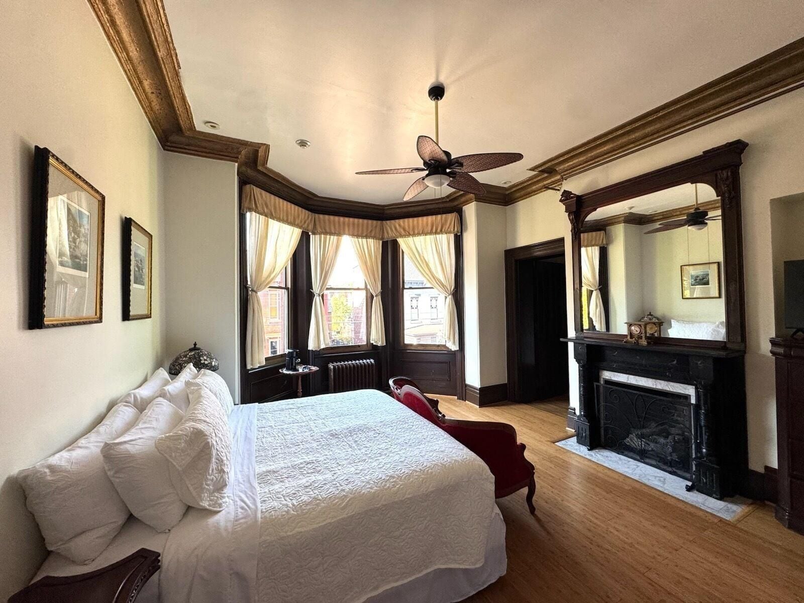 A bedroom with a large bed, a fireplace, and a ceiling fan.