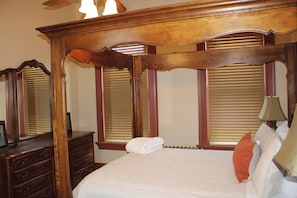 A bedroom with a large wooden headboard, a wooden dresser, a bed with white bedding, and a nightstand with a lamp.