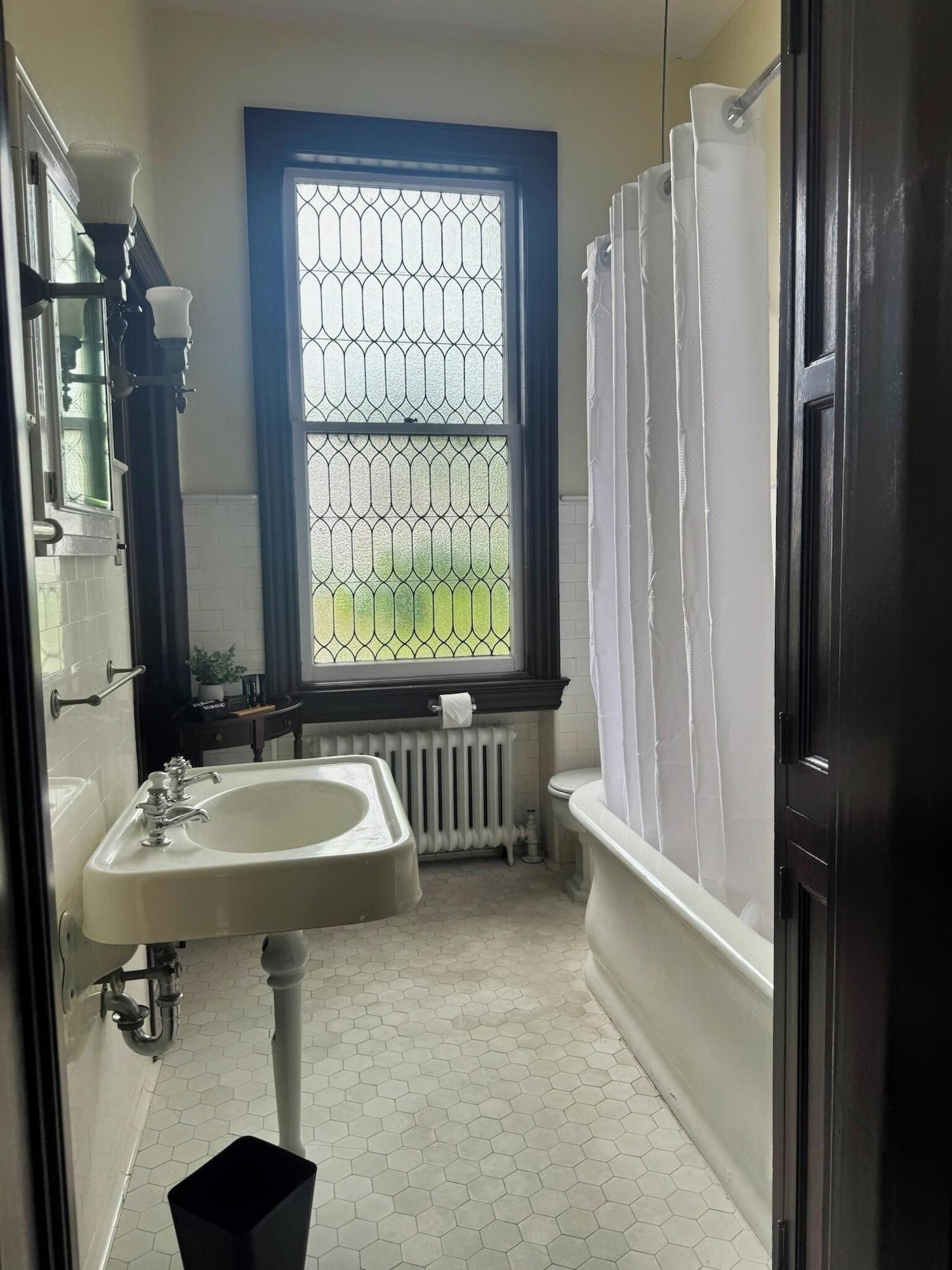 A bathroom with a white sink, a window with a metal grid, a white radiator, and a black door.