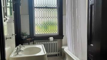 A bathroom with a white sink, a window with a metal grid, a white radiator, and a black door.