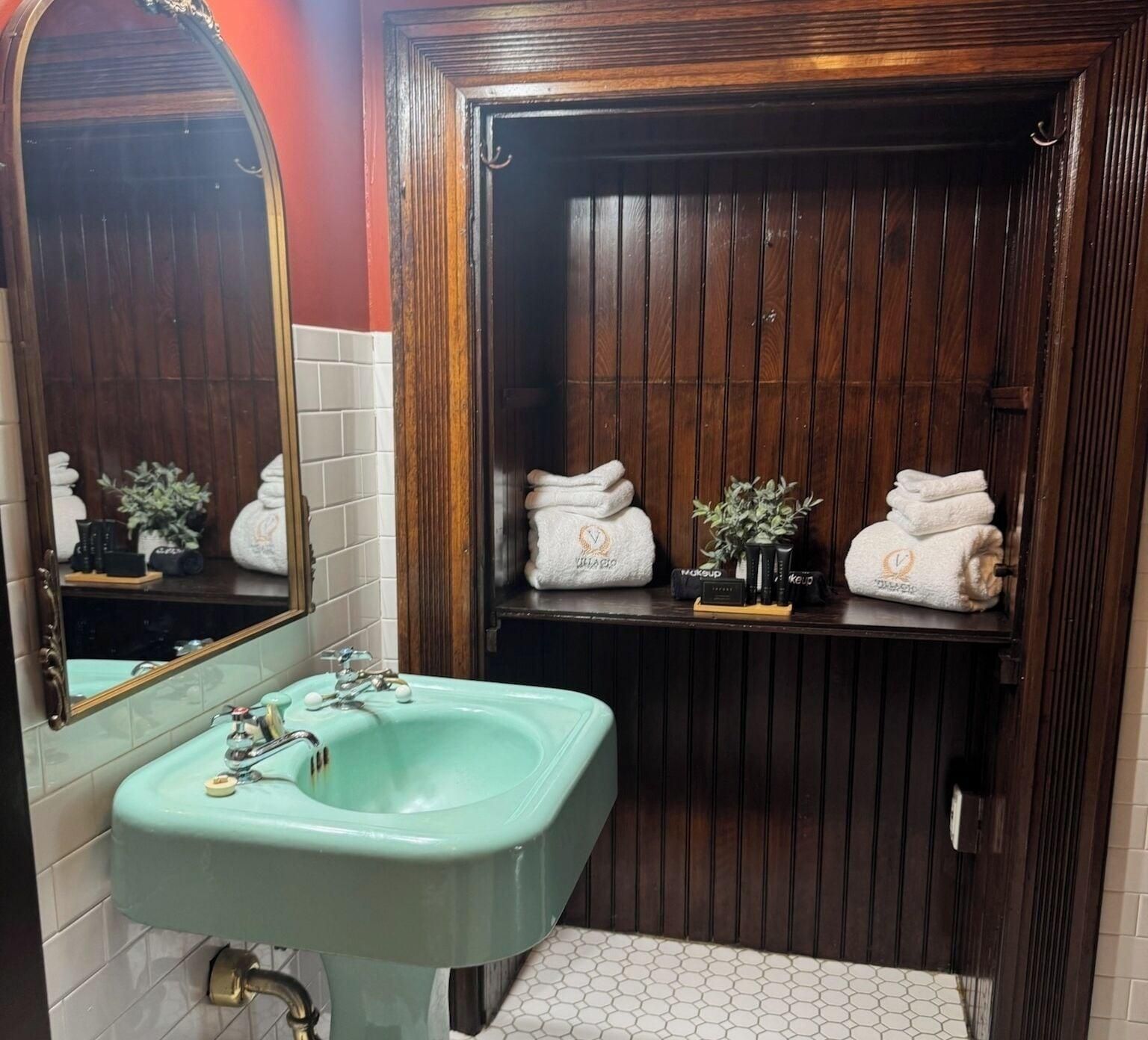 A bathroom with a green sink, wooden vanity, and a mirror.