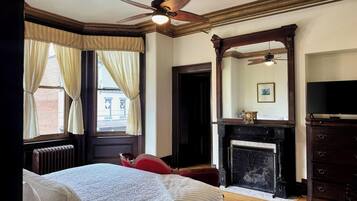 A bedroom with a bed, a fireplace, a mirror, and a ceiling fan.