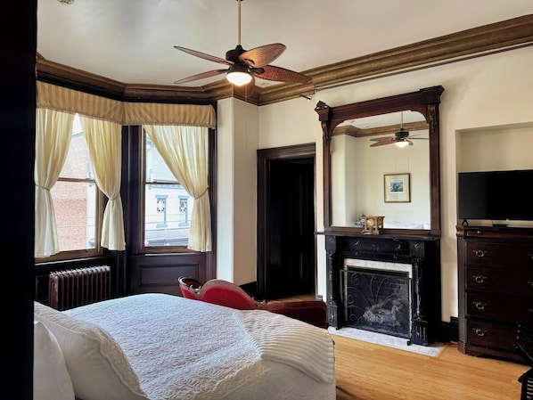 A bedroom with a bed, a fireplace, a mirror, and a ceiling fan.