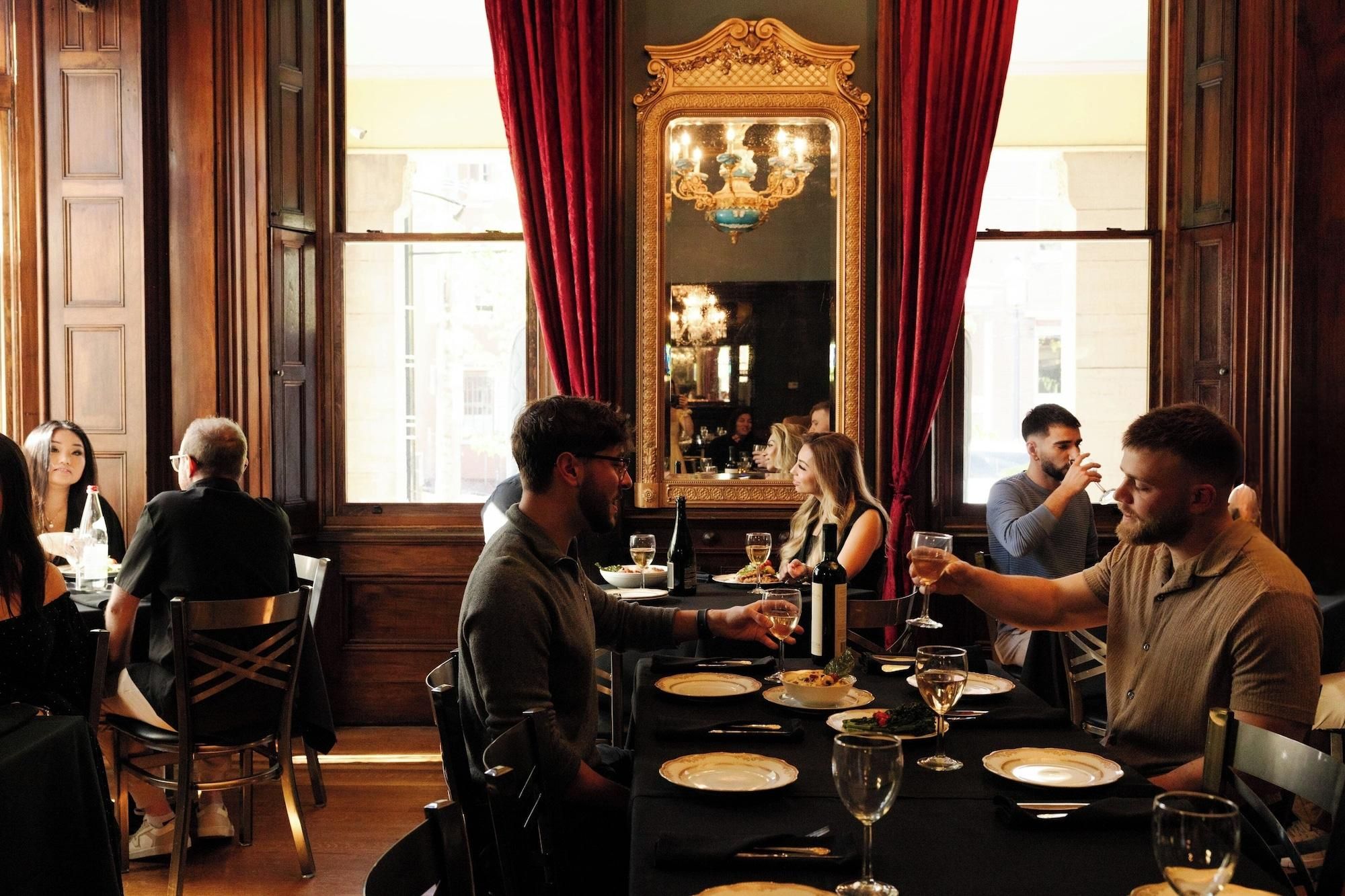 A formal dining room with wooden paneling, a large ornate mirror, and red curtains.