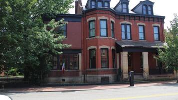 A Victorian-style brick building with a prominent bay window, a covered porch, and a flag on the flagpole.