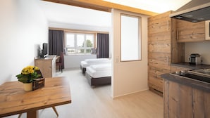 Una habitación de hotel moderna con techo de madera, kitchenette, zona de comedor y cama.