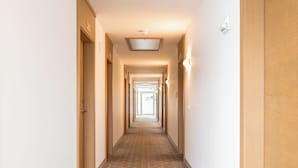 Un pasillo largo y estrecho con puertas de madera a ambos lados, que conduce a una habitación luminosa al final.