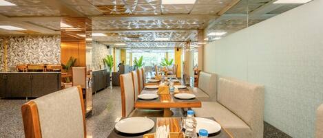 A modern dining area with long tables, cushioned seating, and a patterned ceiling.