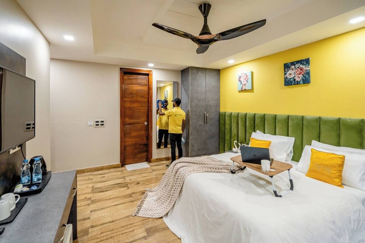 A hotel room with a bed, a desk with a laptop, a TV, and a ceiling fan.