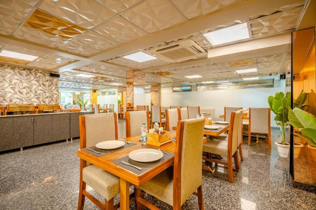 A dining area with multiple tables and chairs, a kitchen in the background, and a decorative ceiling.