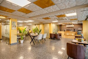 A modern interior with a dining area, a reception desk, and a kitchen. - Lime Tree Hotel - Near Medanta Hospital (Gurugram)