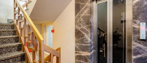 A staircase with wooden railings leading to a room with a marble wall and a glass door.