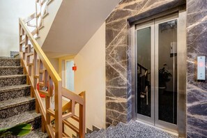 A staircase with wooden railings leading to a room with a marble wall and a glass door. - Lime Tree Hotel - Near Medanta Hospital (Gurugram)
