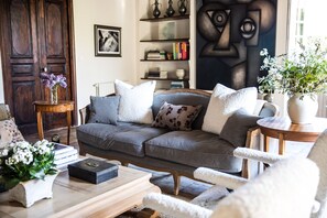 A cozy living room with a grey sofa, white and patterned cushions, a wooden coffee table, and a bookshelf with books and decorative items. - Les Manibelles (Amarens)
