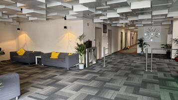 Un vestíbulo moderno con un diseño geométrico en el techo, una recepción y una zona de estar con sofás y sillones.