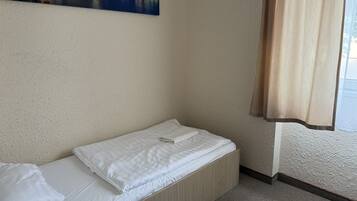 Una habitación pequeña con cama individual, una pared sencilla y un cuadro de un puente.