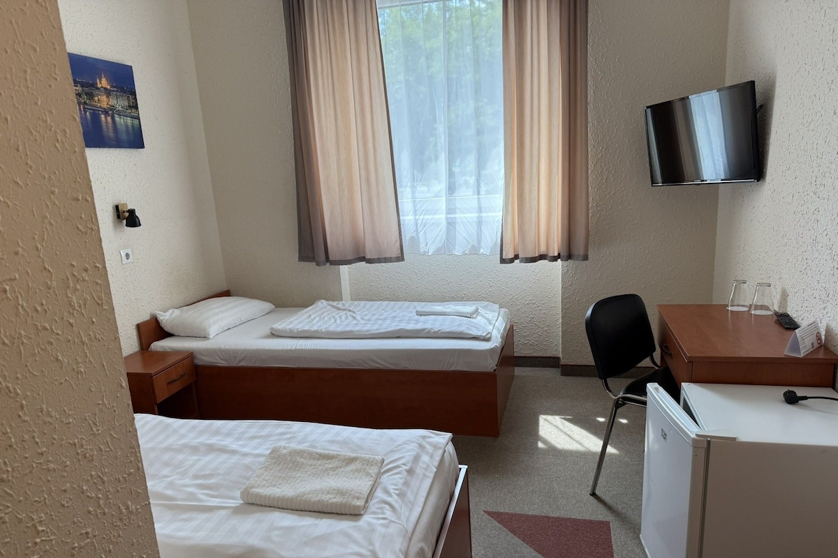 Une chambre d’hôtel avec deux lits, un bureau, une chaise, une télévision et un réfrigérateur.