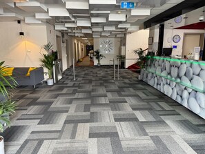Un hall d’hôtel au design moderne, avec un tapis à motifs, un comptoir d’accueil et un escalier menant aux autres étages.