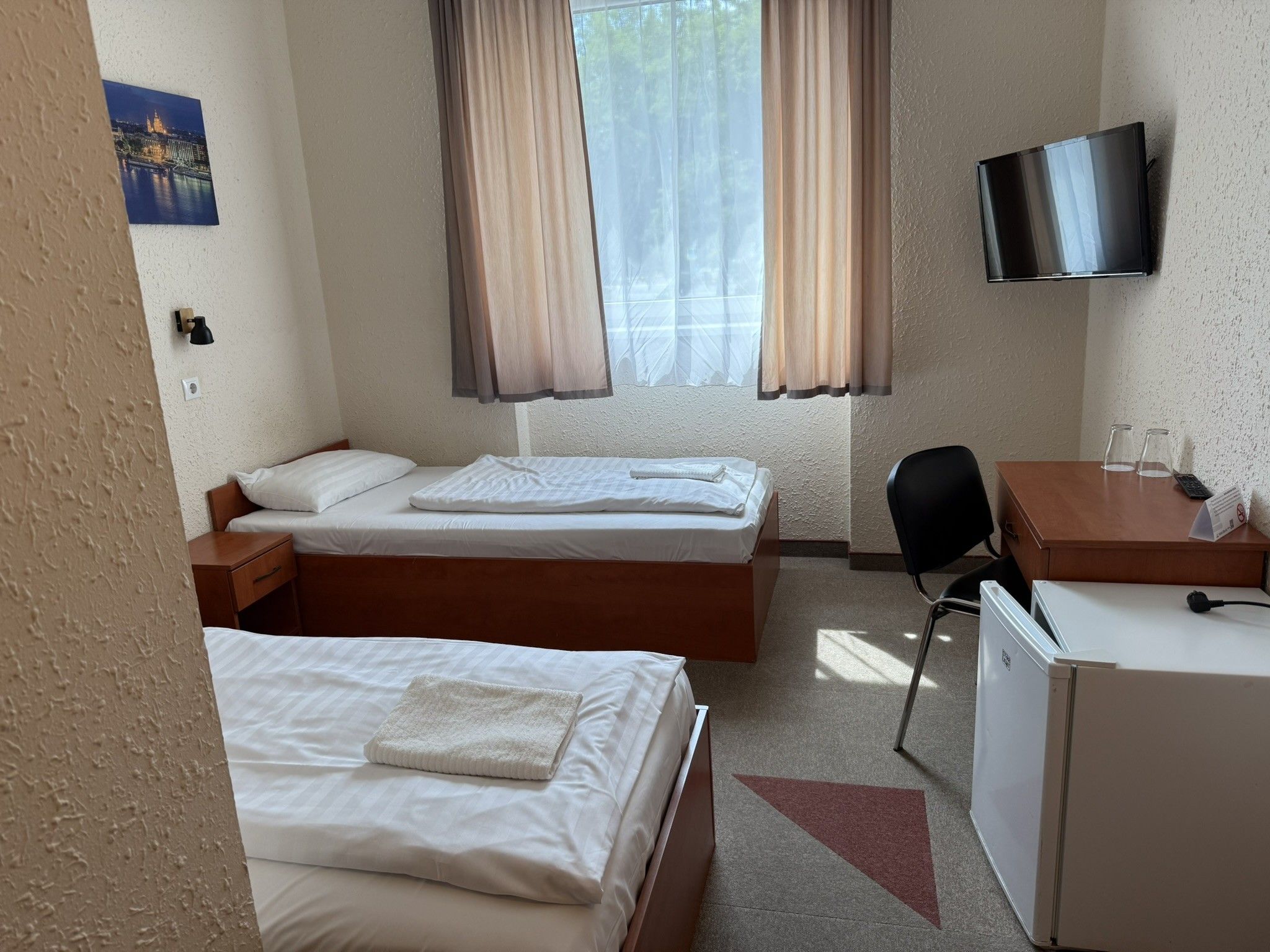 Habitación de hotel con dos camas, un escritorio, una silla, un televisor y un refrigerador.