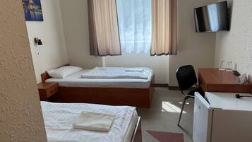 Habitación de hotel con dos camas, un escritorio, una silla, un televisor y un refrigerador.