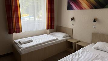 Habitación de hotel con dos camas, una ventana con cortinas translúcidas, una lámpara de pared y un cuadro.