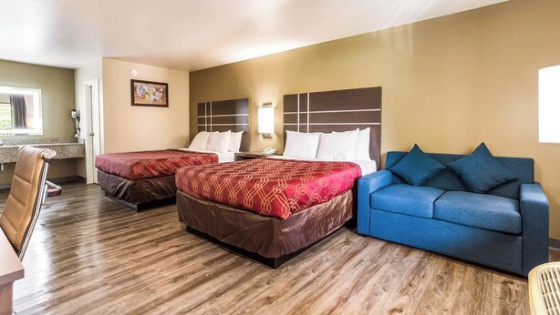A hotel room with two beds, a blue sofa, a desk, and a window.