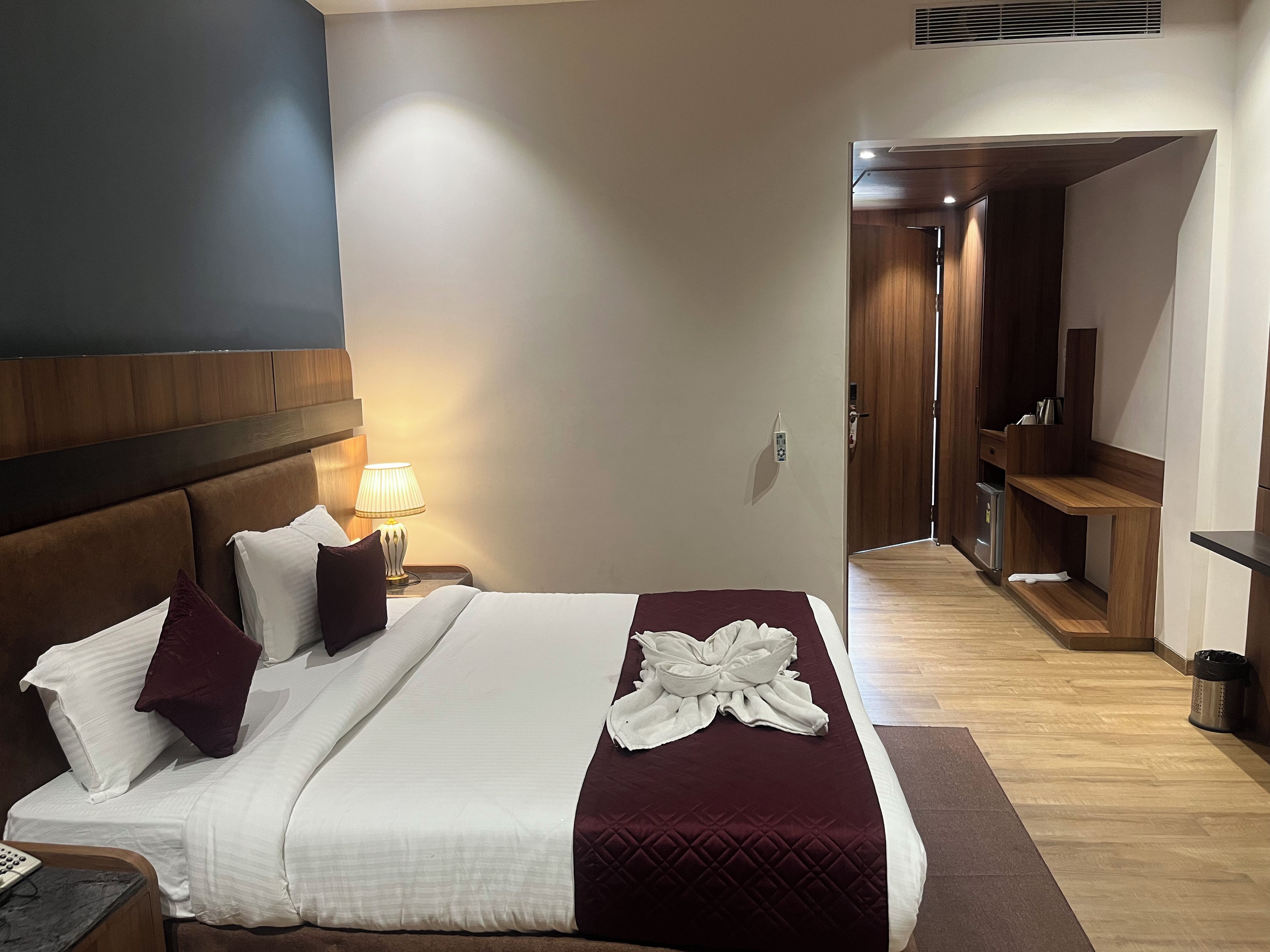 A hotel room with a bed, bedside lamp, and a wooden wardrobe.