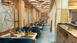 Une grande salle à manger avec des tables disposées pour accueillir de nombreux convives, présentant un design moderne avec des chaises recouvertes de tissu bleu et un îlot central doté d’un comptoir.