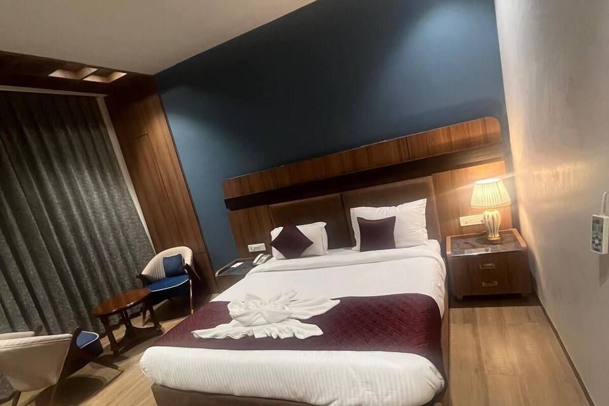 Een moderne hotelkamer met een groot bed, een houten hoofdbord, een nachtkastje met een lamp en een zithoek met een stoel en een klein tafeltje.