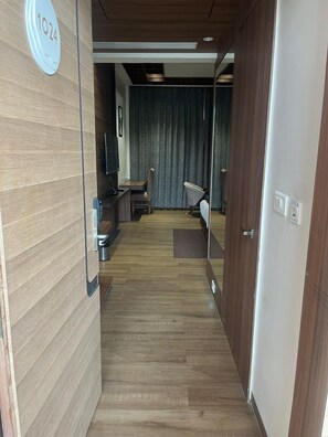 A hotel room with a wooden floor, a desk with a chair, a television, and a curtain. - Nirvana Grand Hotel And Resort (Gaya)