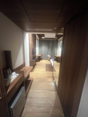 Un pasillo estrecho con un banco de madera a la izquierda, una mesita con una taza y un televisor en la pared.