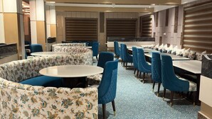 A hotel dining area with round tables, blue upholstered chairs, and patterned cushions. - Nirvana Grand Hotel And Resort (Gaya)