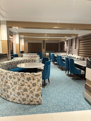 A hotel dining area with round tables, blue upholstered chairs, and patterned cushions. - Nirvana Grand Hotel And Resort (Gaya)