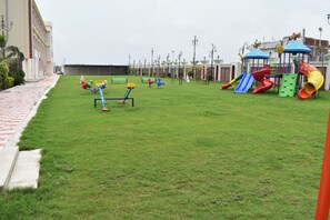Un terrain de jeux équipé de divers jeux, notamment des toboggans et des balançoires, avec en arrière-plan un bâtiment et des lampadaires.