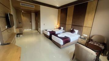 A hotel room with two beds, a desk, a chair, and a television.